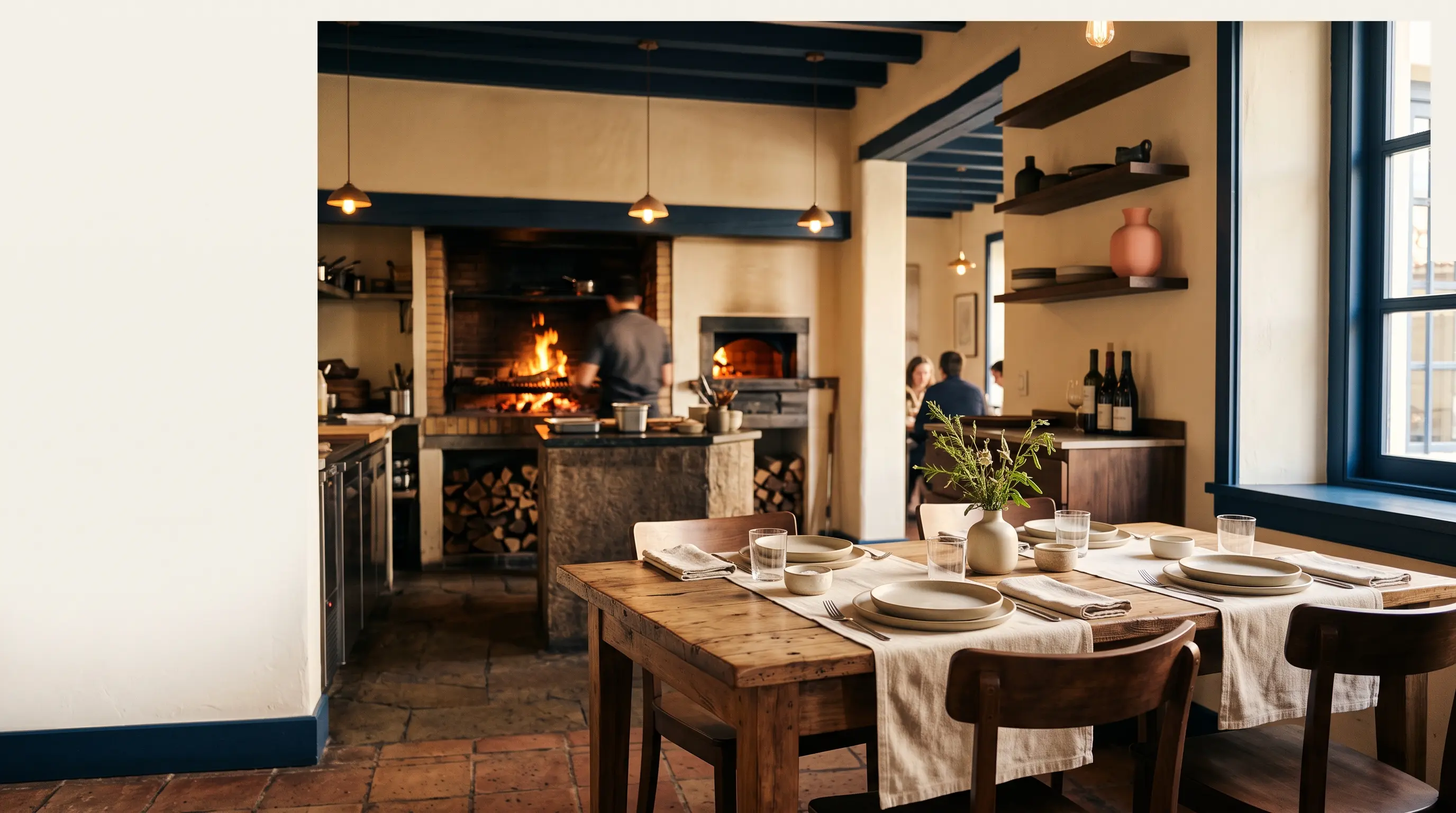 Interior cálido de un restaurante de cocina a la brasa con mesa de madera y parrilla al fondo.